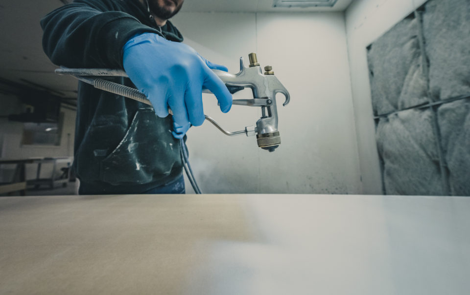 Worker uses a spray gun to apply the final finish on cabinetry.